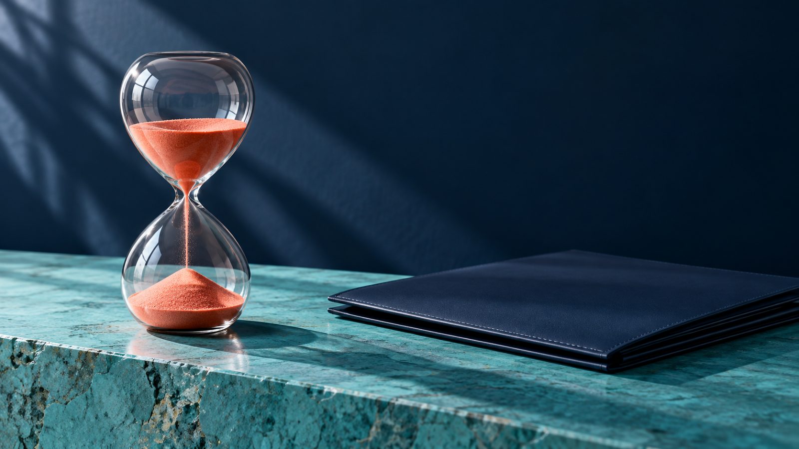 Un sablier au sable corail posé à côté d’un dossier bleu marine évoque le calendrier des versements.